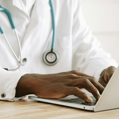 Doctor typing on laptop, stethoscope visible, representing challenges of managing a private practice